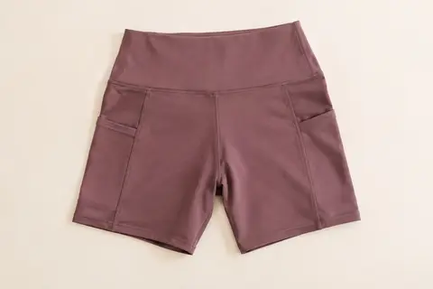 Short de sport COTOP à taille haute et poches latérales, présenté à plat sur un fond ivoire.