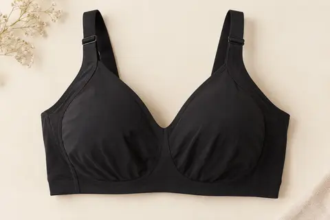 Soutien-gorge minimiseur noir sans armature, posé à plat sur fond ivoire, avec bonnets couvrants et bretelles larges.